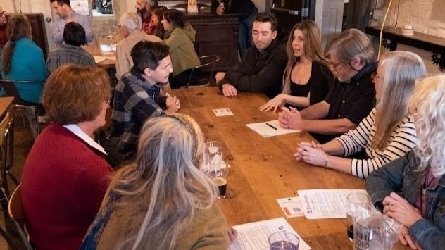 A group of men and women sitting around a wooden table with a series of papers laying on it.