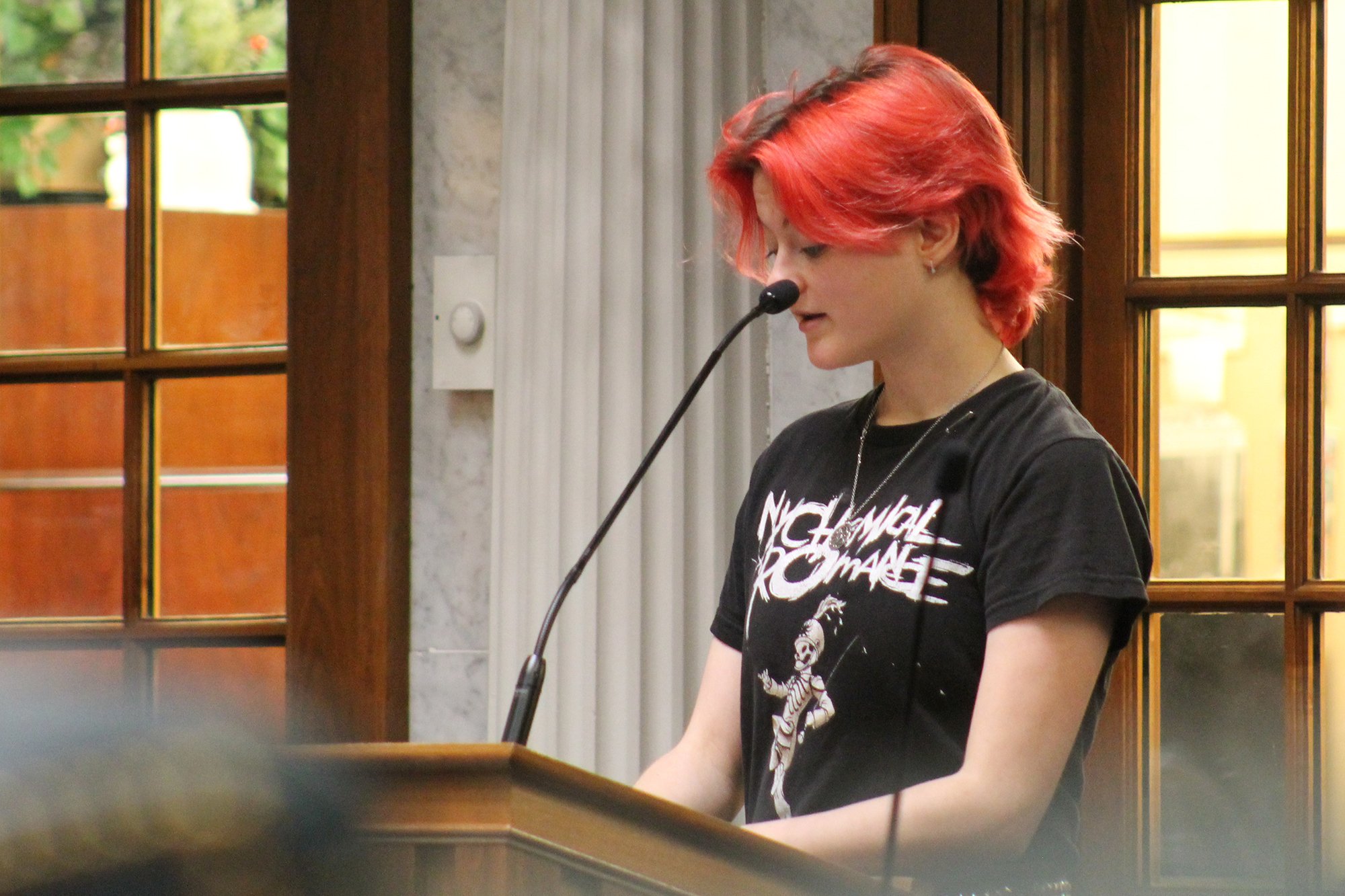 A woman with vibrant red hair speaks at a podium.